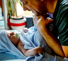 Father smiles at baby wrapped in blue bath towel