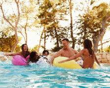 Group of young adults splash and play in a backyard pool.