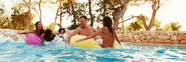 Group of young adults splash and play in a backyard pool.