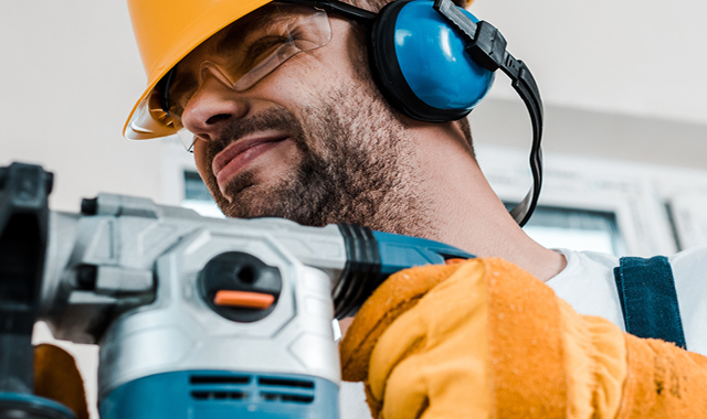 Contractor wears protective helmet, glasses and headphones while sanding