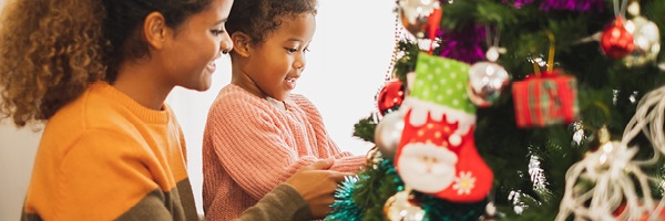 Mother and young daughter decorate a Christmas tree together.