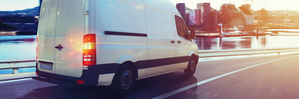 White high roof transit van drives down the road.