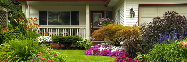 The front yard of a home features several flowerbeds with various flowers and other plants