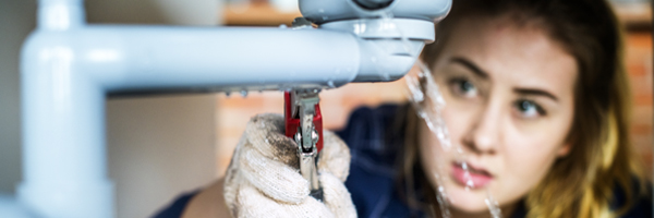 Woman uses tools to fix plumbing under a sink.