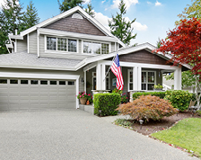 A grey two-story home with white window trim and an American flag hanging off the front porch.