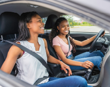 A teenage girl and her mother sit in the front seats of a vehicle with their seatbelts on.