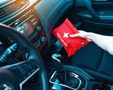 A person in a vehicle with a black interior pulls a red first aid kit from the glove box.