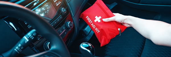 A person in a vehicle with a black interior pulls a red first aid kit from the glove box.