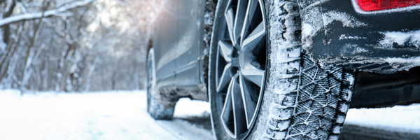 Two tires on a dark vehicle roll over a road that is covered in snow.