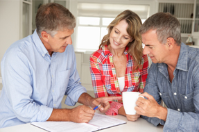 An insurance agent sitting at a table with a man and a woman while discussing a document.