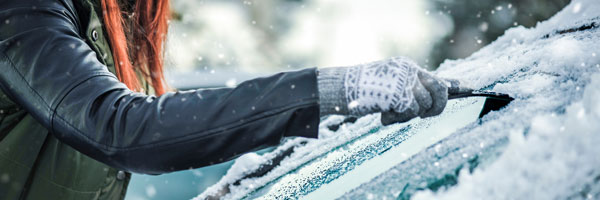 woman scraping ice off of car windshield