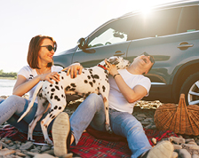 man, woman, and dog sitting by car on a beach