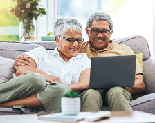 elderly couple sitting on couch looking at laptop